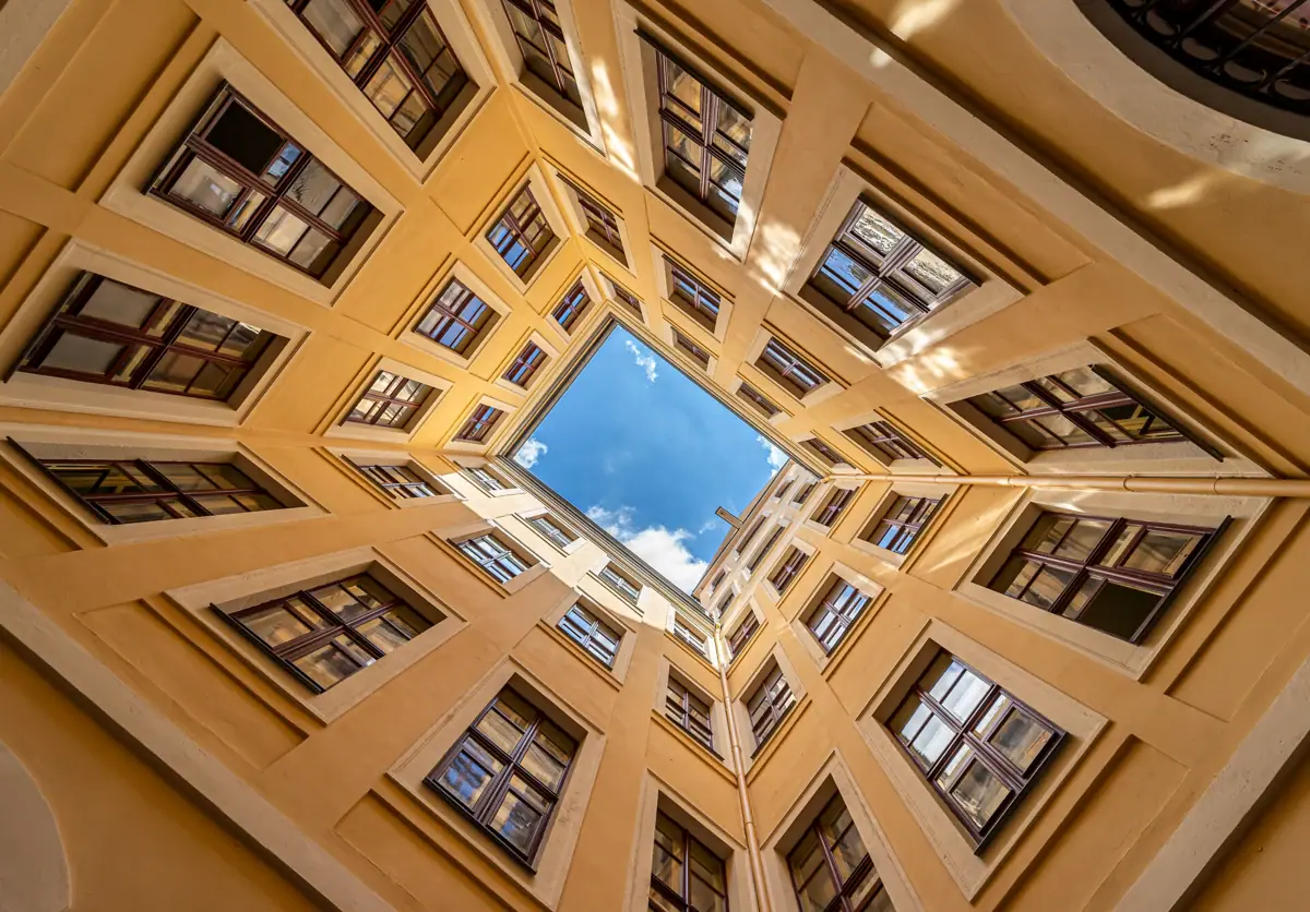 The view from an inner courtyard up to the blue sky with symmetrical windows.