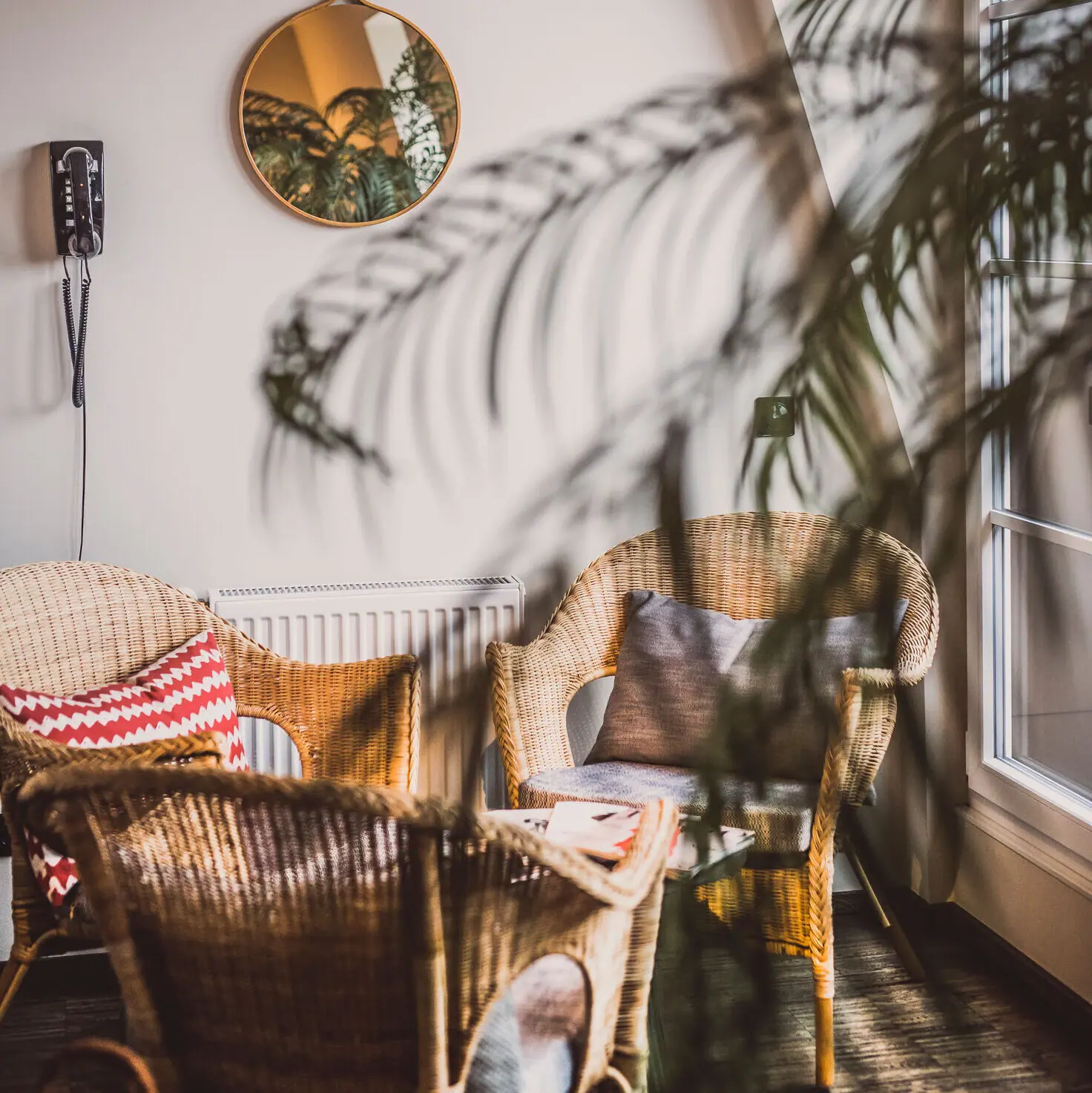 Wicker chairs with cushions in front of a white wall with a mirror.