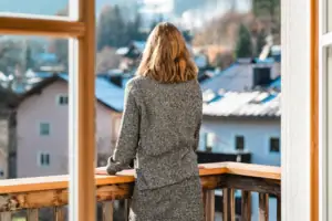 A woman looks out of a window at a mountain range.