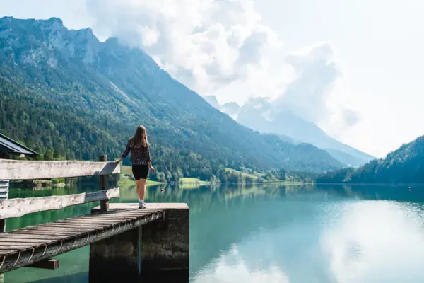 A woman stands on a jetty and looks out over a lake.