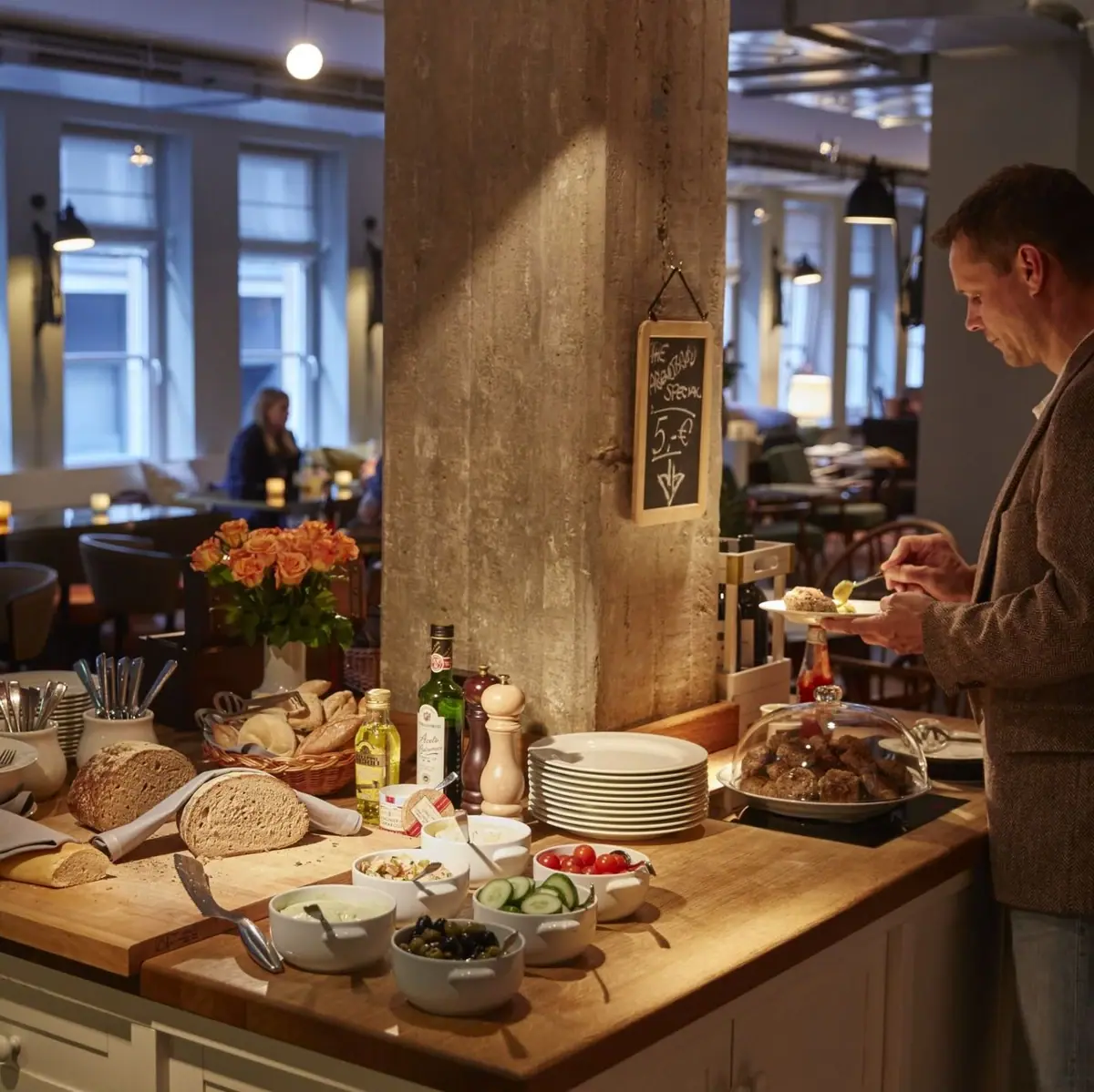 A man stands at a bar eating dinner and puts something on his plate.