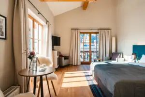 Spacious room with table and double bed, flooded with light from the many windows.