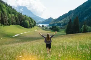 A woman is standing in a field with her arms raised.