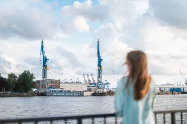 A woman stands at a religious building and looks across the Elbe towards Hamburg harbour