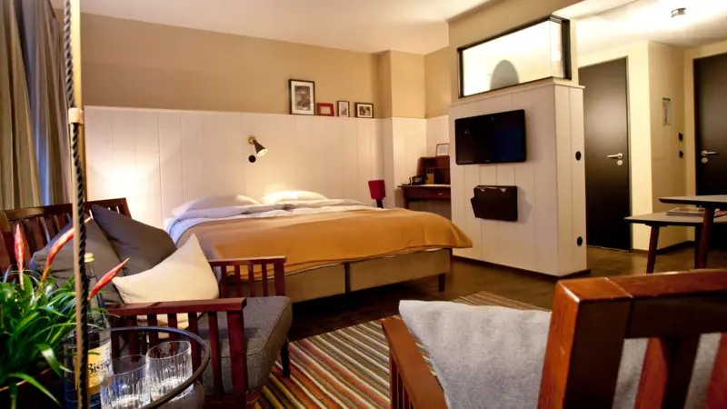 Room with double bed with yellow bedspread and seating area with small table and armchairs