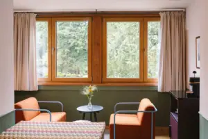 A seating area with two armchairs in front of a window in the Chambre hotel room at the HENRI Hotel Garmisch-Partenkirchen.