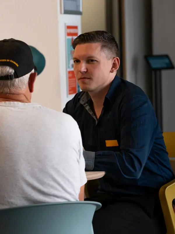 A man is sitting at a table with another man in a white shirt.