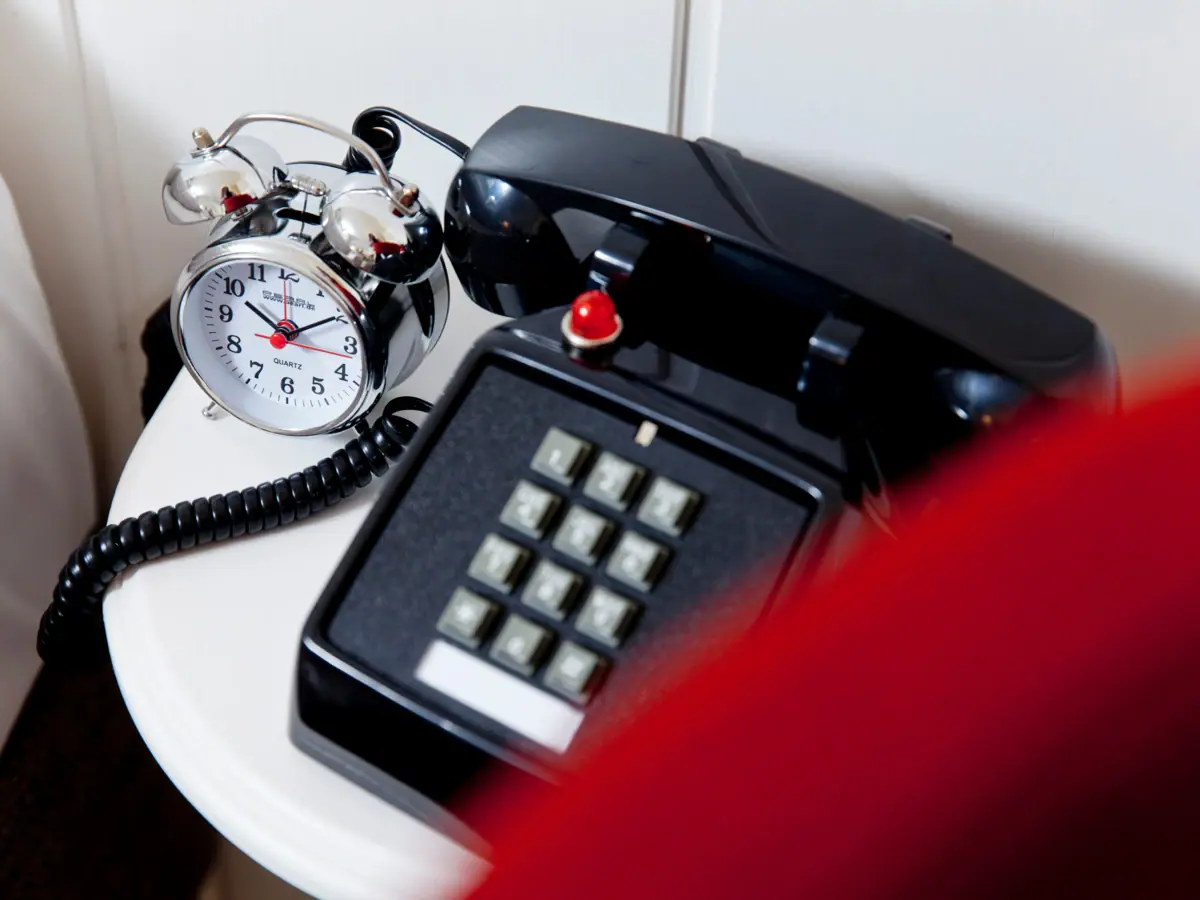 Retro telephone and silver alarm clock on a white side table