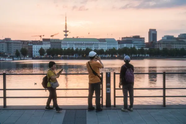 A group of people are standing on a pavement next to a body of water.